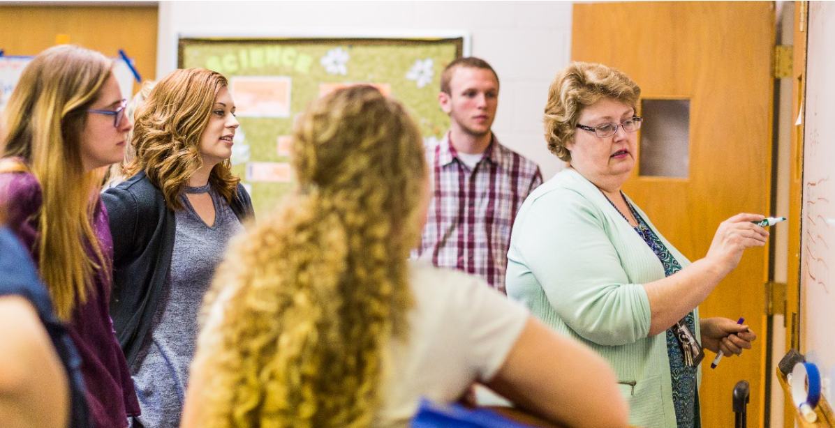 An instructor speaking with a group of students while writing on a dry erase board
