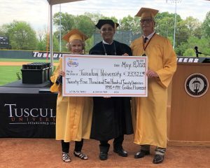 Three people in graduation attire holding a large symbolic check