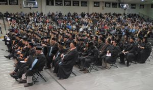 A crowd in graduation attire sits in rows of chairs