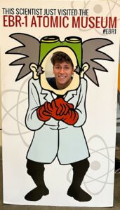 Young man posing behind a photo opportunity cut out of a cartoon scientist